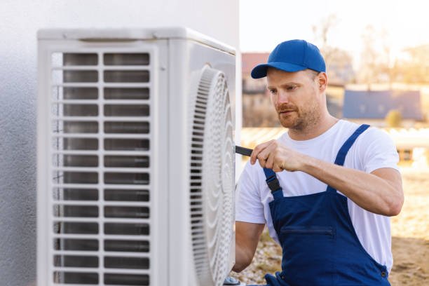 A technician in overalls performs HVAC maintenance in Cooper City, FL, repairing an air conditioner for optimal performance.
