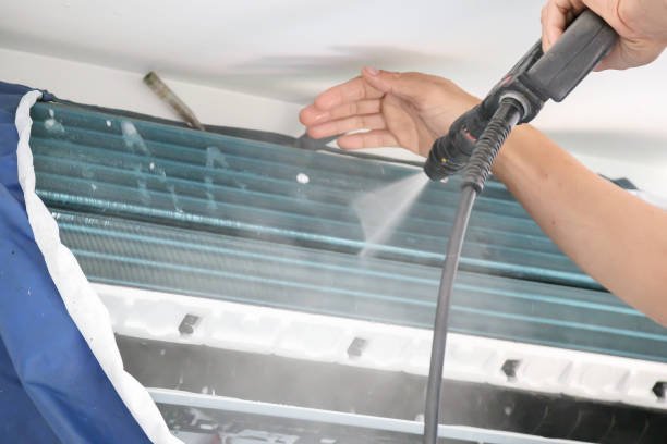 A person sprays a window air conditioner with a water hose for cleaning, ensuring proper maintenance and efficient AC coil cleaning.